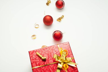 Hediye kutusu kırmızı, altın bir yay ile parlak, altın kurdeleler ve Noel toplarıyla süslenmiş, beyaz arka planda, yazıtlar için bir yer var. Yeni yıl ya da Noel için hediye kavramı.