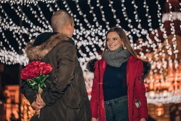 Young man hiding a bouquet of roses from his girlfriend at night — Stock Photo, Image