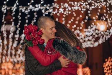 Kadın bir buket gül tutuyor ve ona sarılırken gülümsüyor