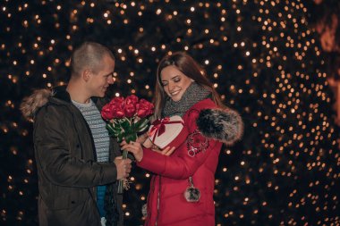 Genç bir kadın elinde bir hediye kutusu ve güller tutarken