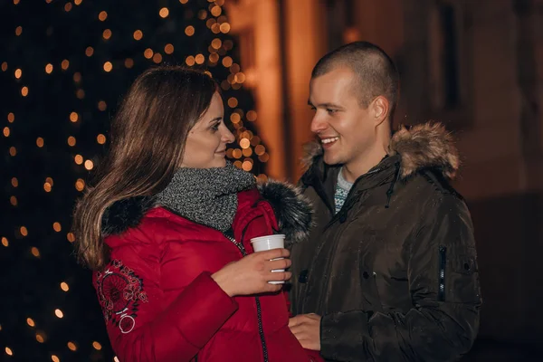 Jong gelukkig paar met warme dranken, omarmen 's nachts — Stockfoto