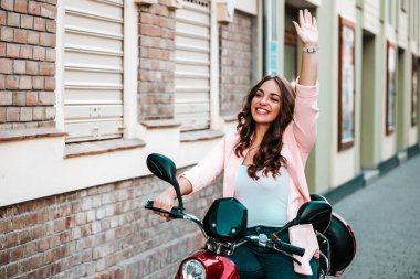 Scooter 'a binerken elini sallayan güzel genç bir kadın.