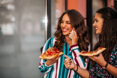 İki güzel genç bayan dışarıda pizza yiyip sohbet ediyorlar..