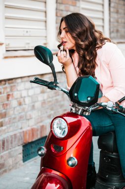 Bir kadın aynaya bakarken ruj sürüyor.