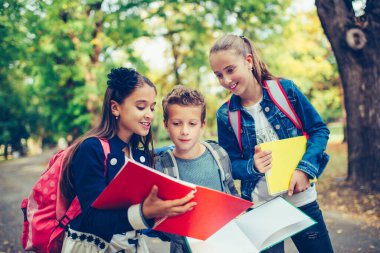 Group of kids with backpacks are having fun, talking, reading a 