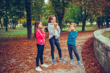 Üç mutlu çocuk dışarıda pizza yiyip sohbet ediyor.