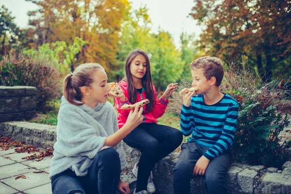 Gruppe von drei lächelnden Kindern, die miteinander reden und Pizza essen — Stockfoto