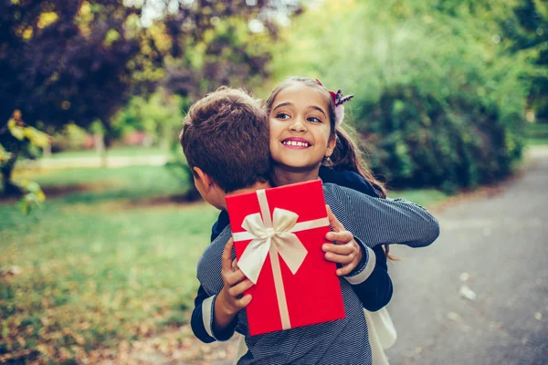 Happy little girl is holding gift in red box and smiling while h