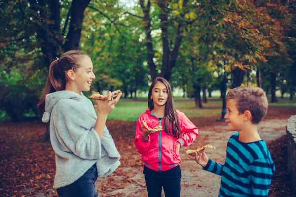 Tre bambini felici ridono, parlano e mangiano pizza all'aperto — Foto Stock