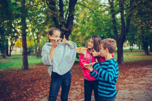 Drei glückliche Kinder, die draußen reden und Pizza essen — Stockfoto