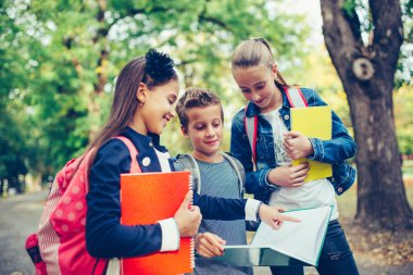 Group of kids with backpacks are having fun, talking, reading a 