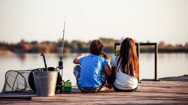 Güneşli bir yaz gününde, gölde sandviç yiyip balık tutan iki küçük sevimli arkadaş. Çocuklar oynuyor. Arkadaşlık..