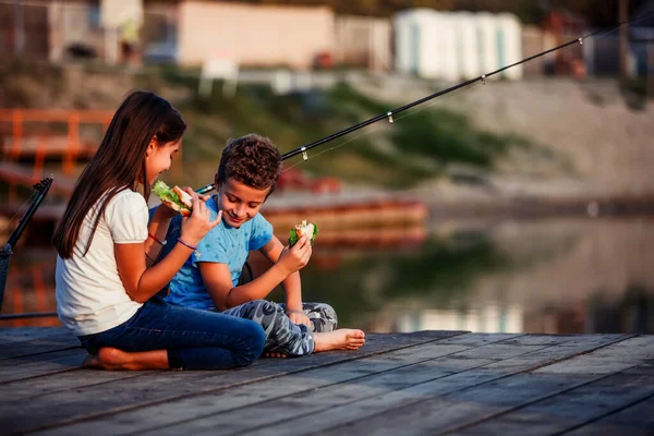 两个年轻可爱的小朋友 男孩和女孩聊天 吃三明治 在阳光明媚的夏日在湖里钓鱼 孩子们在玩友谊 — 图库照片