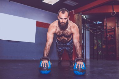 Genç sakallı adam spor salonunda kettlebell ağırlıkları ile pushup yapıyor