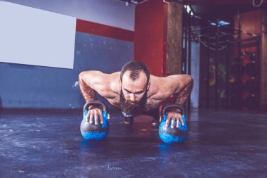 Genç sakallı adam spor salonunda kettlebell ağırlıkları ile pushup yapıyor