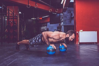 Çıplak gövdeli genç sakallı adam spor salonunda kettlebell ağırlıklarıyla şınav çekiyor.