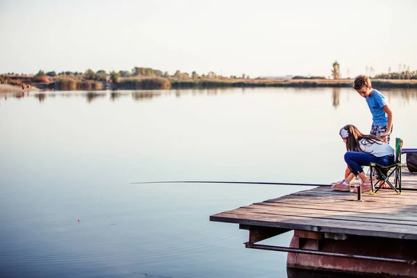 Two young cute little friends, boy and girl fishing on a lake in a sunny summer day. Kids are playing. Friendship.