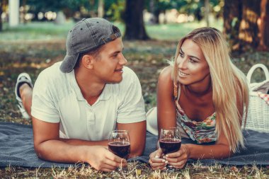 Güzel genç çift konuşuyor, gülüyor ve parkta romantik bir piknikte bir kadeh şarap içiyor.