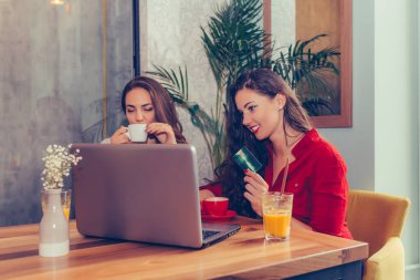 Kahve içip internetten kredi kartı ve kafede oturan dizüstü bilgisayarla alışveriş yapan iki heyecanlı bayan arkadaş..