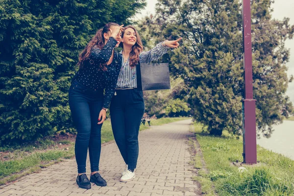 買い物の後 公園を歩く2人の女性の親友 通りで微笑んで指差す — ストック写真