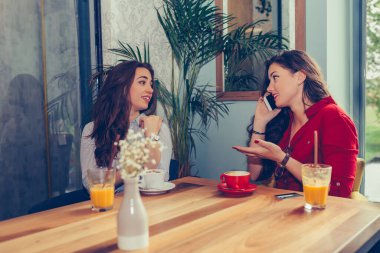 Heyecanlı iki genç kadın, arkadaşlarıyla bir cep telefonu aracılığıyla bir buluşma ayarlıyor. Kadın saati kontrol ediyor..