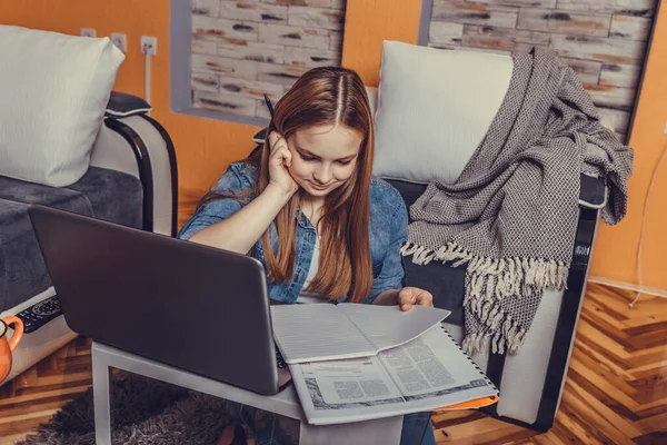 Beautiful girl studying with a laptop on line, learning and writing notebook in living room at home