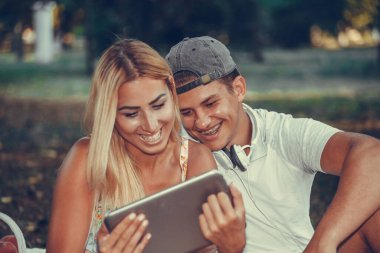 Parkta piknik yaparken dijital tablete bakan mutlu bir çiftin fotoğrafı..