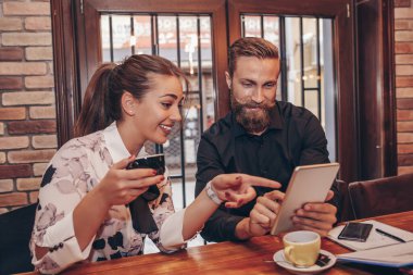 İş adamları dijital tablet kullanıyor, konuşuyor, kahve içiyor ve kafede çalışırken gülümsüyor..