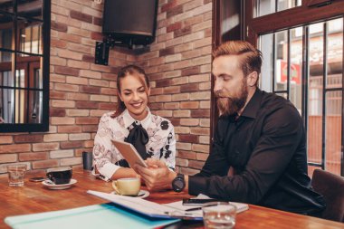 İki iş arkadaşından oluşan bir ekip, kafede otururken tablet kullanarak yeni projeyi tartışıyor..