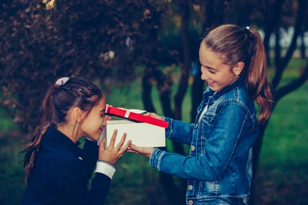 Child giving gift box to friend. Happy little girl opening gift in a red box. People, children, holidays, friends and friendship concept