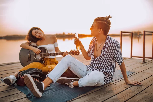 幸せな若いカップルのビールを飲み ギターを演奏し 川の歌 — ストック写真