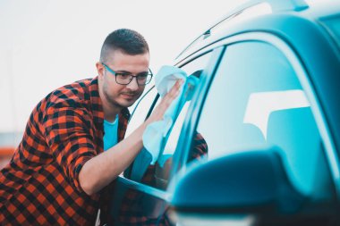 Tatmin olmuş bir gencin portresi. Arabasını bezle temizliyor ve şişeye sıkıyor..