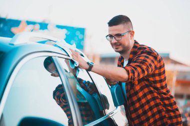 Arabasını mikrofiber bezle temizleyen ve şişeye sprey sıkan mutlu bir gencin fotoğrafı..