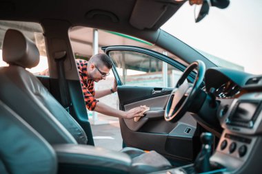 Genç adam arabasının içini bir paçavrayla dikkatlice temizliyor..