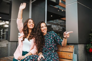 Mutlu, duygusal, genç ve güzel bir arkadaşın görüntüsü. Kadın dışarıda, sokakta oturuyor ve birine el sallıyor.