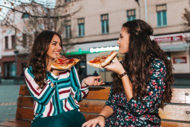 Açık havada pizza yiyip konuşan ve eğlenen iki genç kadının portresi. Yaşam tarzı, modern hayat..