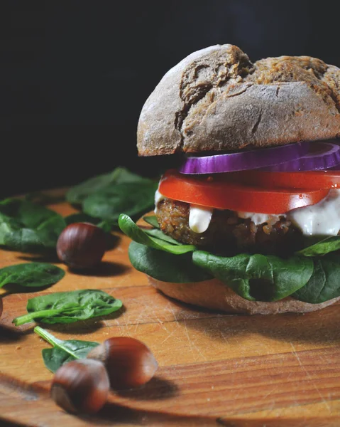 veggie, vegan burger with buckwheat, tomato, onion, vegan mayonnaise and spinach on a fresh bun with flax seeds and sesame, surrounded by spinach leaves