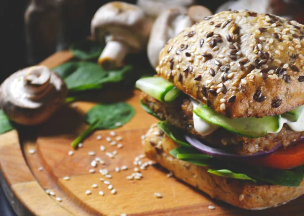 veggie, vegan burger with buckwheat, tomato, onion, vegan mayonnaise and spinach on a fresh bun with flax seeds and sesame, surrounded by spinach leaves, mushrooms, tomato, black pepper and spices.