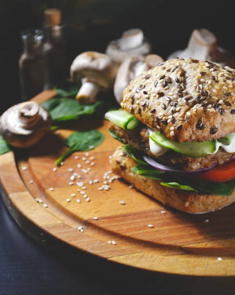 veggie, vegan burger with buckwheat, tomato, onion, vegan mayonnaise and spinach on a fresh bun with flax seeds and sesame, surrounded by spinach leaves, mushrooms, tomato, black pepper and spices.