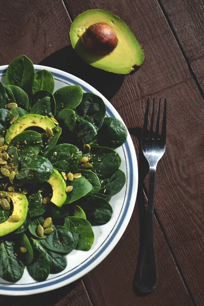 Useful salad with avocado, spinach and pumpkin seeds, seasoned with olive oil and lemon juice. Healthy food.