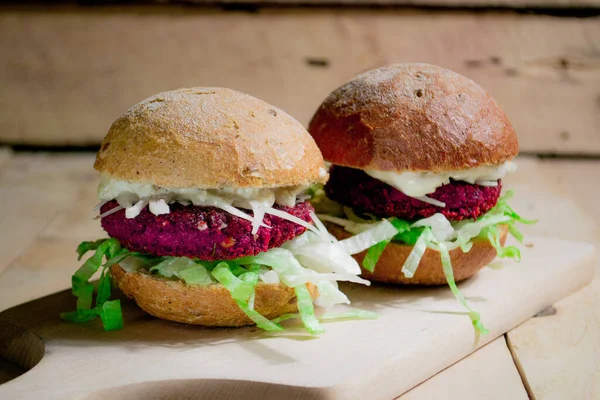 Vegan burger from beet falafel. Vegan burger with a pink chop, fresh salad and mayonnaise of soy milk on a wooden background. Falafel in the form of heart