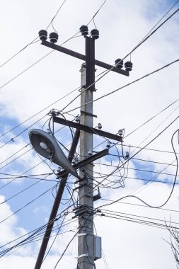 Elektrik yalıtıcıları ve fener ışıkları, gökyüzünün arka planında bulutlarla kaplanmış elektrik kablolarının yüksek elektrik desteğini yakıyor..