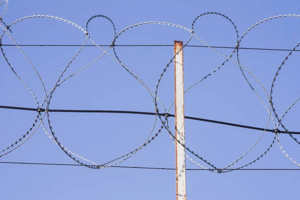 Coiled razor wire with its sharp steel barbs on top of a wire mesh perimeter fence ensuring safety and security preventing access or the escape of prisoners blue sky background