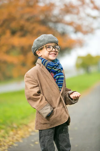 Το κομψό χαριτωμένο αγόρι σε ζεστά ρούχα στο φθινοπωρινό τοπίο — Φωτογραφία Αρχείου
