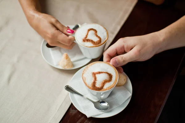 Loving couple hands in a cafe drinknig coffee with heart shape decoration