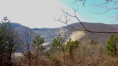 Taş ocağının manzarası güneşli bir günde uzaklardan görünen bir dağı kesiyor..