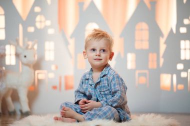 Sevimli sarı saçlı küçük çocuk pijama yakınındaki Noel oyuncak kağıt evler.