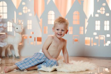 Sevimli sarı saçlı küçük çocuk pijama yakınındaki Noel oyuncak kağıt evler.