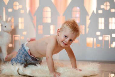 Sevimli sarı saçlı küçük çocuk pijama yakınındaki Noel oyuncak kağıt evler.