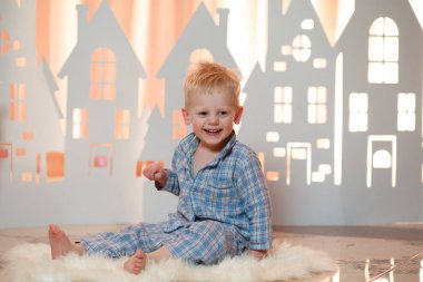 Sevimli sarı saçlı küçük çocuk pijama yakınındaki Noel oyuncak kağıt evler.